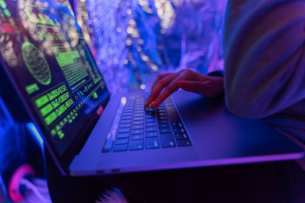 Close-up side angle shot of a person using a laptop with green text and a digital globe on the screen.